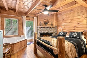 Een houten chalet van binnen met een stenen openhaard, een bed met beddengoed met een patroon, een houten bureau en een raam met jaloezieën.