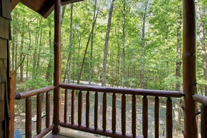 A wooden deck with a railing overlooking a forested area with a river. - 3 Brothers Bears | Smoky Mountain Escape (Sevierville)