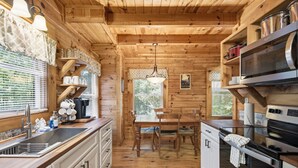 A wooden cabin interior with a kitchen, dining area, and a window with blinds. - 3 Brothers Bears | Smoky Mountain Escape (Sevierville)