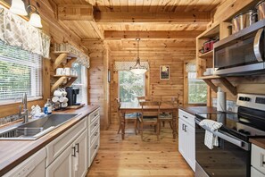 Interior de uma cabana de madeira com cozinha, sala de jantar e janela com persianas.