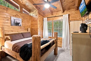 A wooden cabin room with a bed, a desk, a television, and a window with curtains. - 3 Brothers Bears | Smoky Mountain Escape (Sevierville)