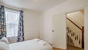 Ein Schlafzimmer mit einem Bett, einem Vorhangfenster, einem Heizkörper und einer Treppe, die zu einer weiteren Etage führt.