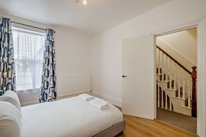 Ein Schlafzimmer mit einem Bett, einem Vorhangfenster, einem Heizkörper und einer Treppe, die zu einer weiteren Etage führt.