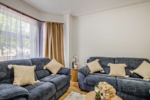 A living room with two grey sofas, beige cushions, a small wooden side table, and a vase with flowers. - Host & Stay | Venetian Retreat (Great Yarmouth)
