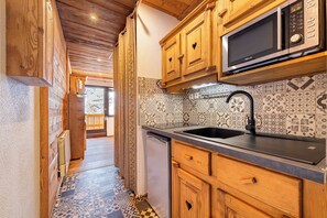 A kitchen with wooden cabinets, a microwave, a sink, and patterned backsplash tiles. - Residence Les Olympiades, Ski In-Out with WiFi in Val Thorens, “V5” by Versant Collection (Val Thorens)