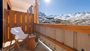 Ein Holzbalkon mit einem weißen Stuhl und einem kleinen Tisch, mit Blick auf ein verschneites Bergmassiv.