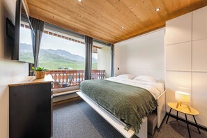 A bedroom with a bed, a bedside table, a lamp, and a view of mountains through a window. - Residence Dôme de Polset, Ski In-Out with WiFi in Val Thorens, “V13” by Versant Collection (Val Thorens)