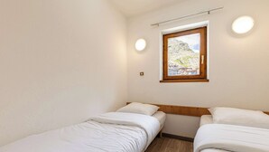 Ein kleiner, sauberer Raum mit zwei Einzelbetten, einem Fenster mit Blick auf eine Berglandschaft und einer Deckenleuchte.