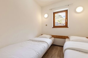 A small, clean room with two single beds, a window with a view of a mountainous landscape, and a ceiling light fixture. - Residence Altineige, Ski In-Out with WiFi in Val Thorens, “V10” by Versant Collection (Val Thorens)