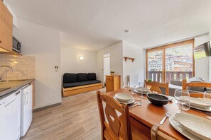 A compact kitchen with modern appliances, a dining area with wooden furniture, and a view of a mountainous landscape through large windows. - Residence Altineige, Ski In-Out with WiFi in Val Thorens, “V10” by Versant Collection (Val Thorens)