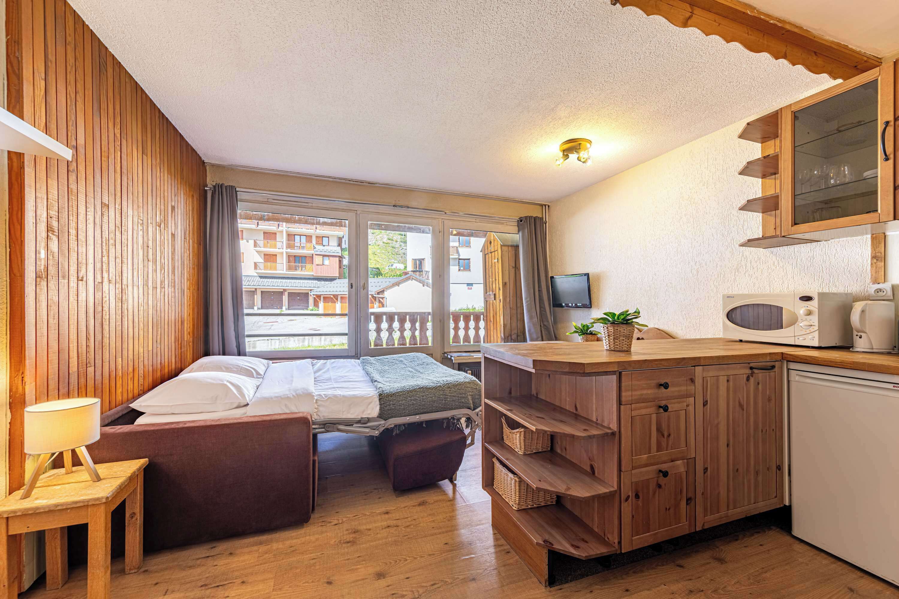 Una habitación funcional con cama, un escritorio pequeño, kitchenette y vistas al exterior.