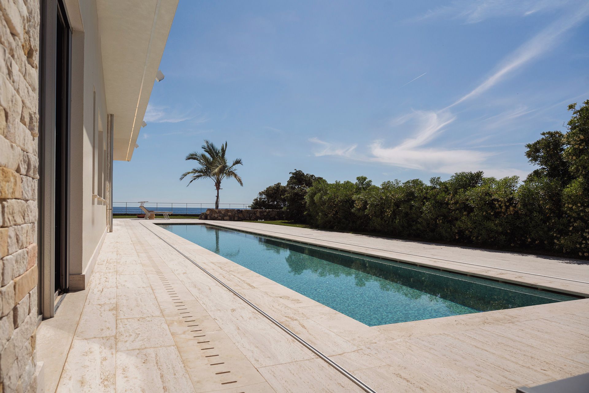 A swimming pool with a clear view of the ocean, a palm tree, and a stone wall.