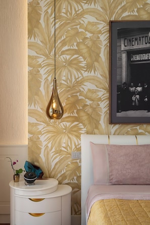 Een slaapkamer met een bed, nachtkastje, een wandlamp, een lijst met afbeelding en tropisch behang.