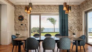 A dining area with a large table and six chairs, a view of the ocean, and a tropical plant outside.