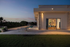 Een modern huis met een zwembad, buiten zitplaatsen en een eethoek.