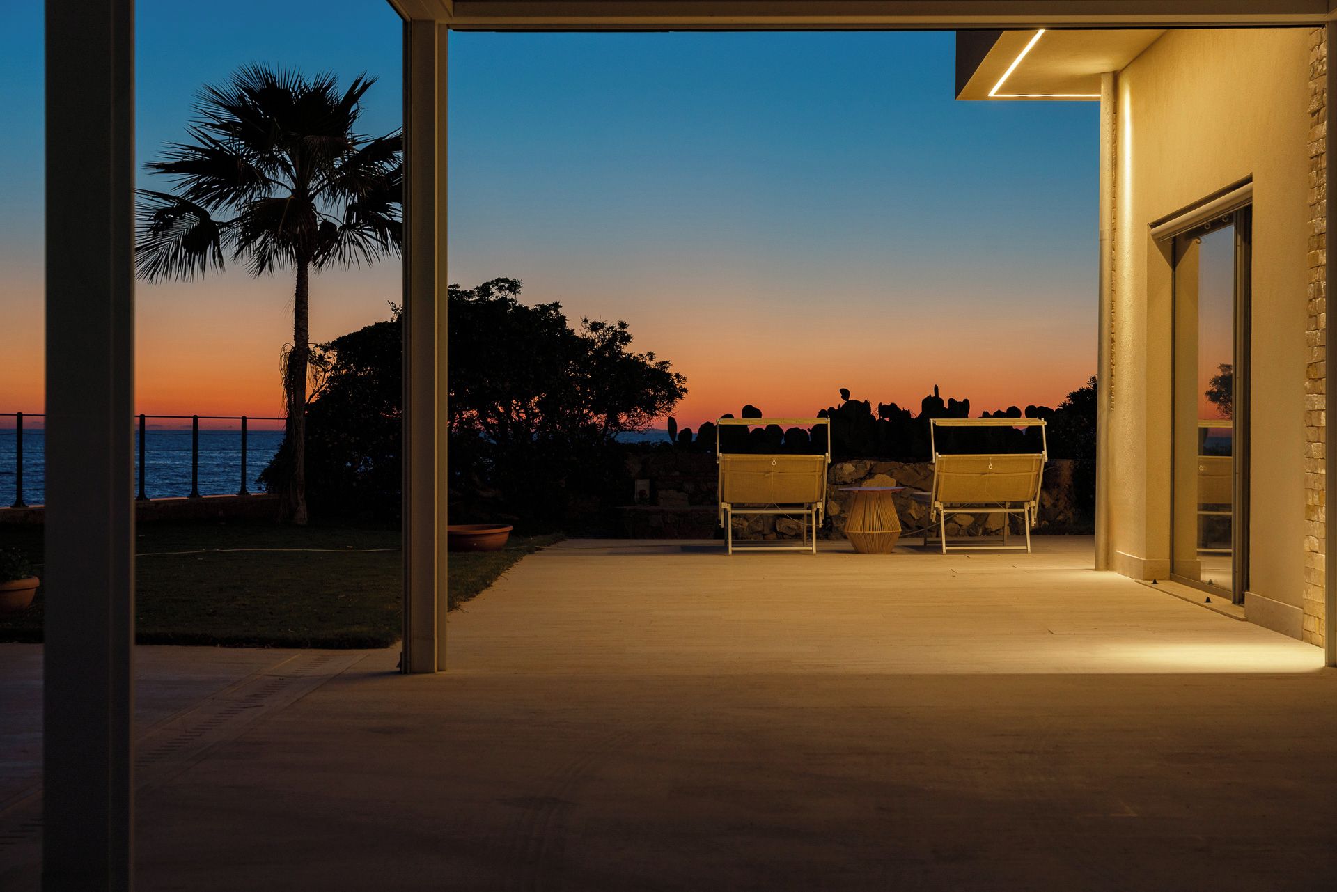 An outdoor patio with two chairs and a table, overlooking a sunset over the sea.