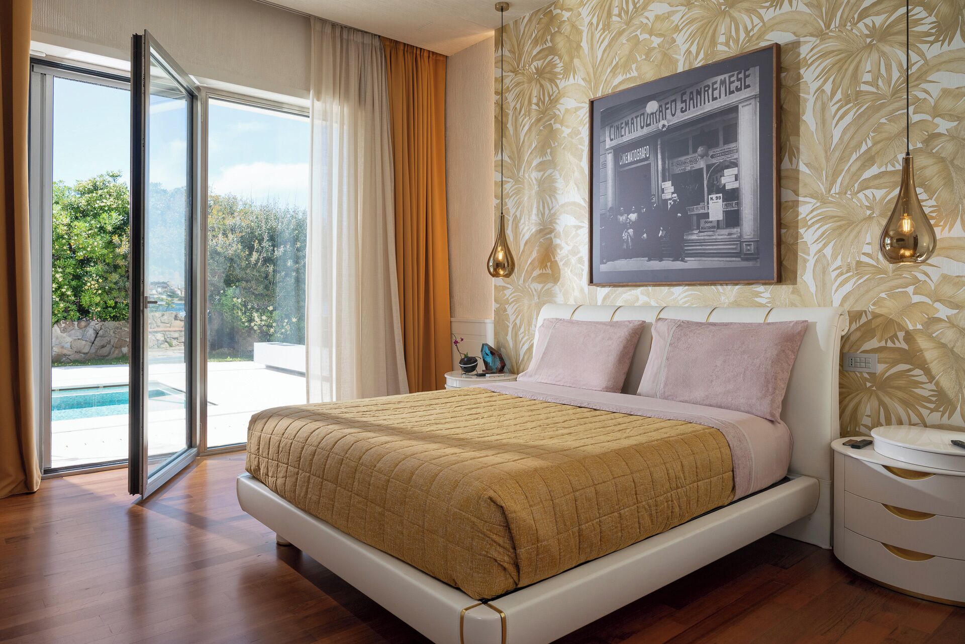 Una camera da letto con un letto, un comodino, una lampada, un quadro incorniciato e vista su una piscina.
