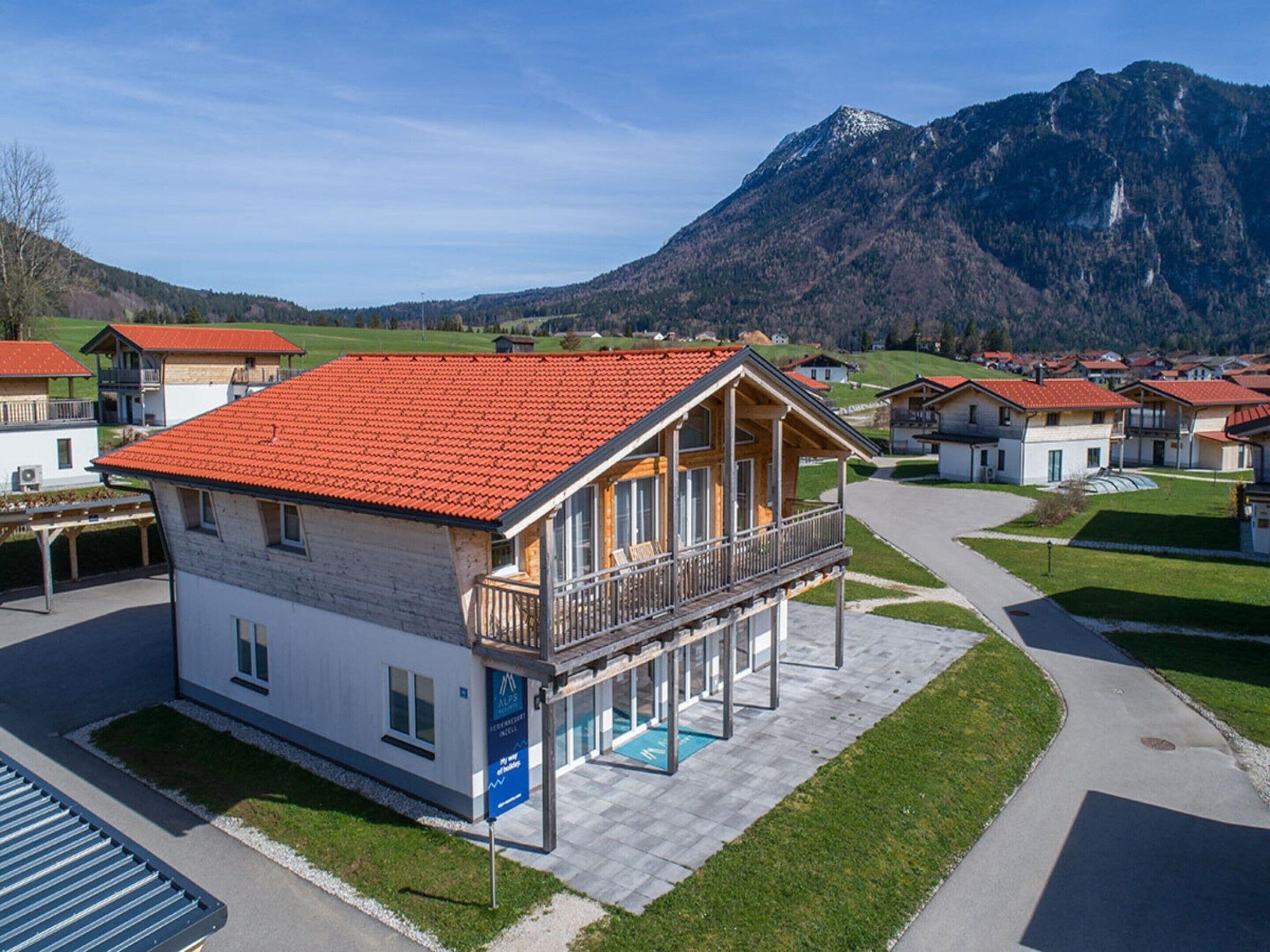 Ein modernes Chalet mit rotem Ziegeldach, einem Balkon und einem Poolbereich.