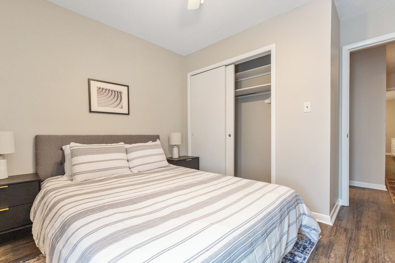 Une chambre à coucher comprenant un lit, des tables de chevet, un tableau encadré, une armoire et une porte donnant sur une autre pièce.