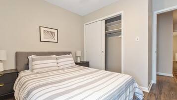 Une chambre à coucher comprenant un lit, des tables de chevet, un tableau encadré, une armoire et une porte donnant sur une autre pièce.