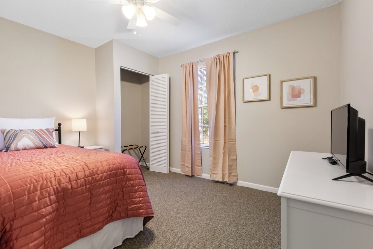 A bedroom with a bed, a desk, a television, and a ceiling fan.