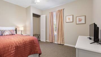 A bedroom with a bed, a desk, a television, and a ceiling fan.