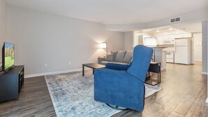 Un salon avec un fauteuil bleu, une table basse et un téléviseur posé sur un meuble.