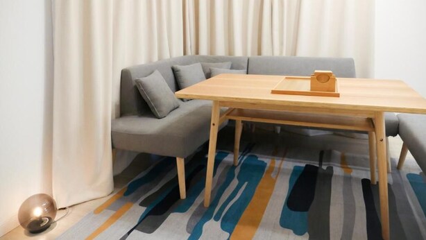 Une pièce avec une table en bois, un canapé gris et un tapis à motifs.