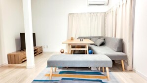 Un espace de vie moderne avec un canapé gris, une petite table en bois, un banc et un tapis coloré.