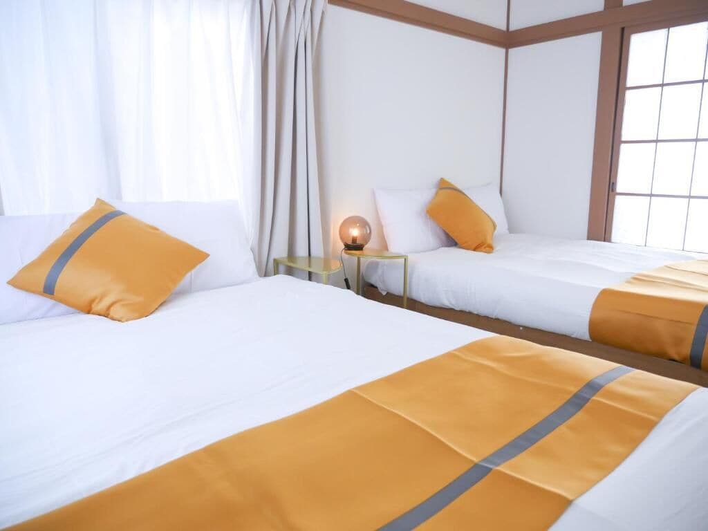 A hotel room with two beds, a nightstand with a lamp, and a window with curtains.