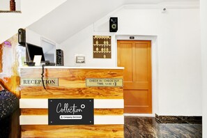 Un mostrador de recepción de hotel con un cartel de recepción, un cartel de registro de entrada y salida, y un cartel con el número de habitación.
