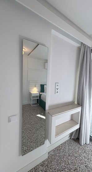 Ein Hotelzimmer mit großem Spiegel, Nachttisch, Bett und Fenster mit Vorhängen.
