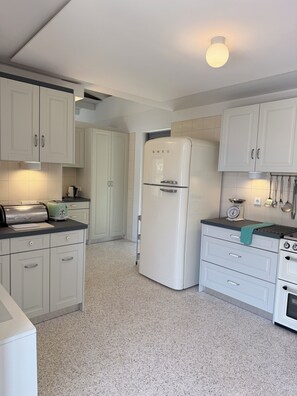 A kitchen with white cabinets, a white refrigerator, a stove, and a countertop with a kettle and a scale.
