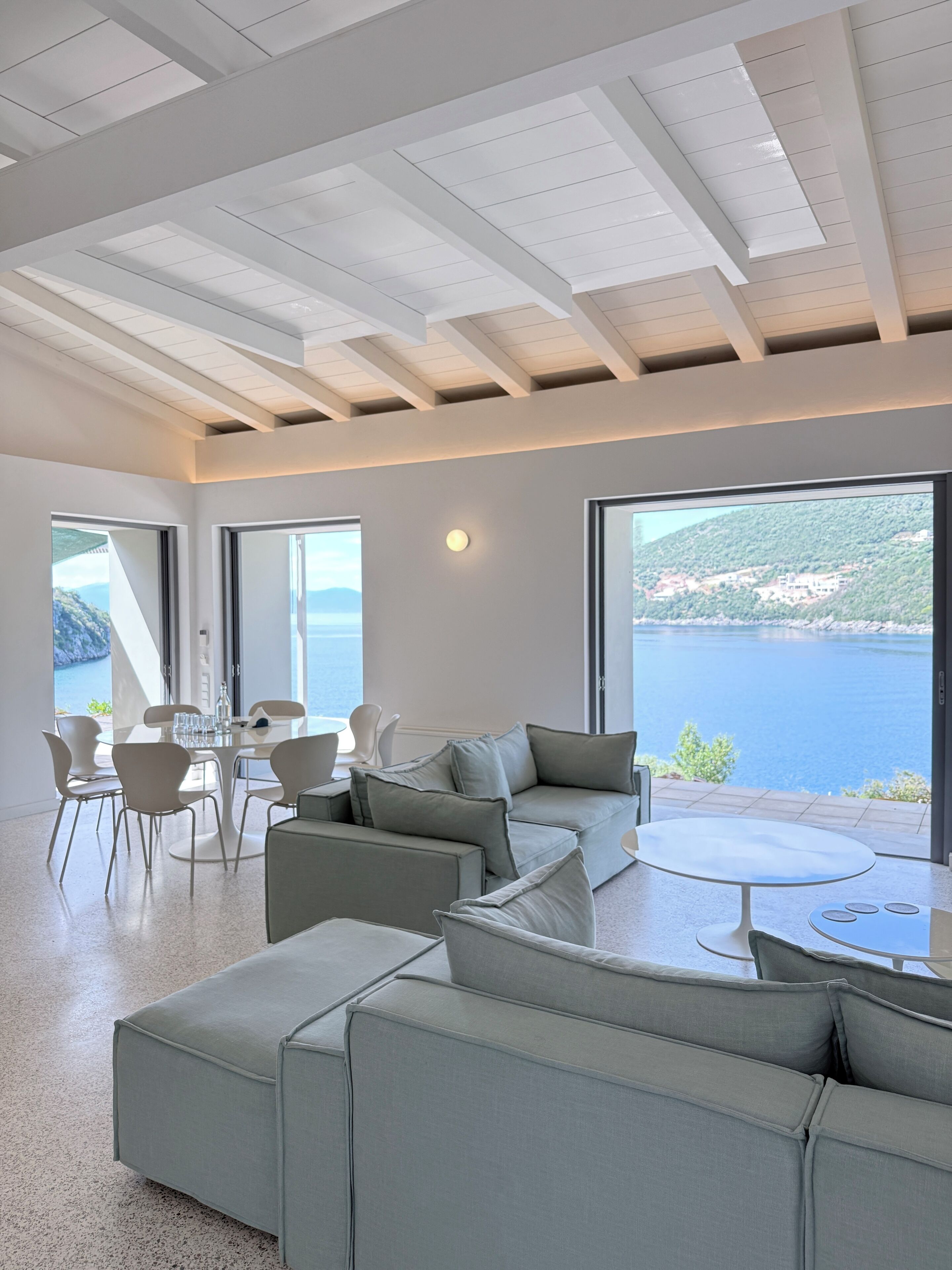 Ein modernes Wohnzimmer mit einer großen Couch, einem Esstisch mit Stühlen und Meerblick durch große Fenster.