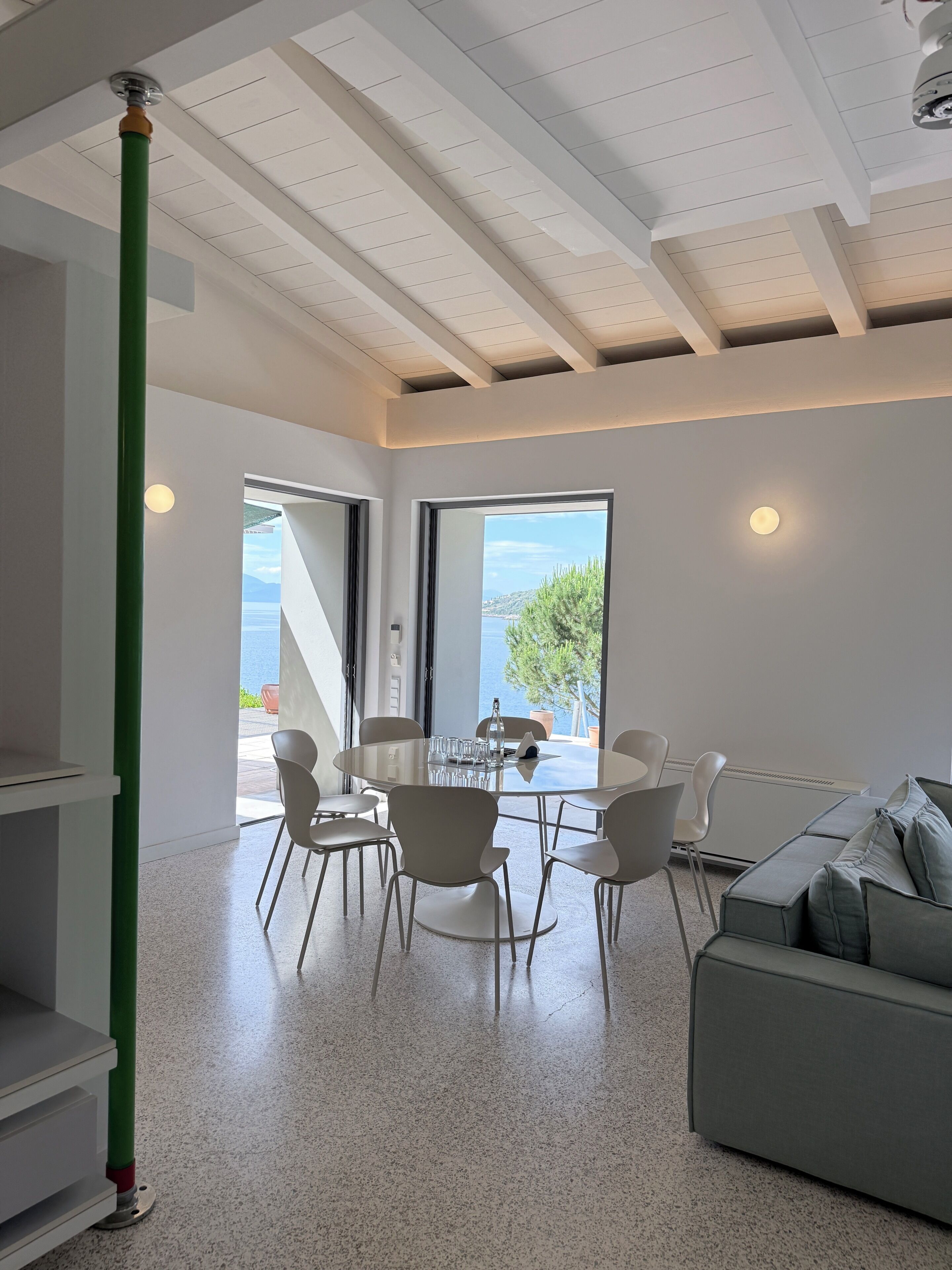 A modern interior with a dining area, a sofa, and a view of the sea.