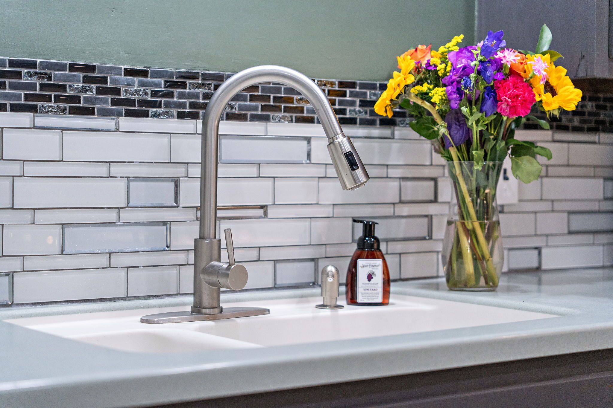 A kitchen sink with a modern faucet, a soap dispenser, and a vase with colorful flowers on the counter.