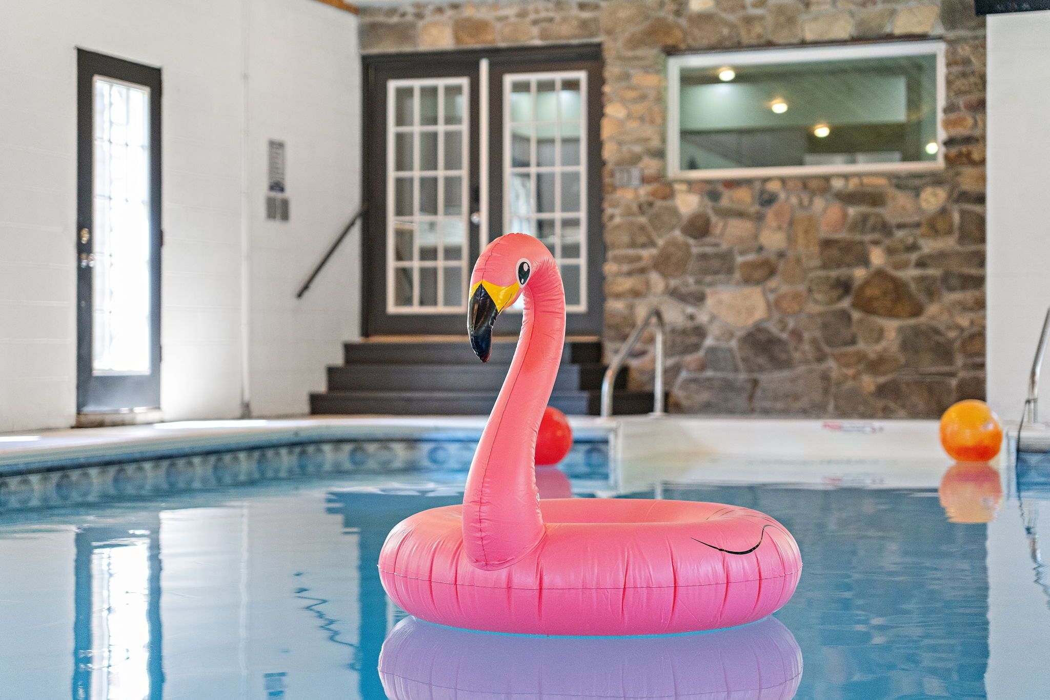 Un flamenco inflable rosa en una piscina con paredes de piedra y una puerta al fondo.
