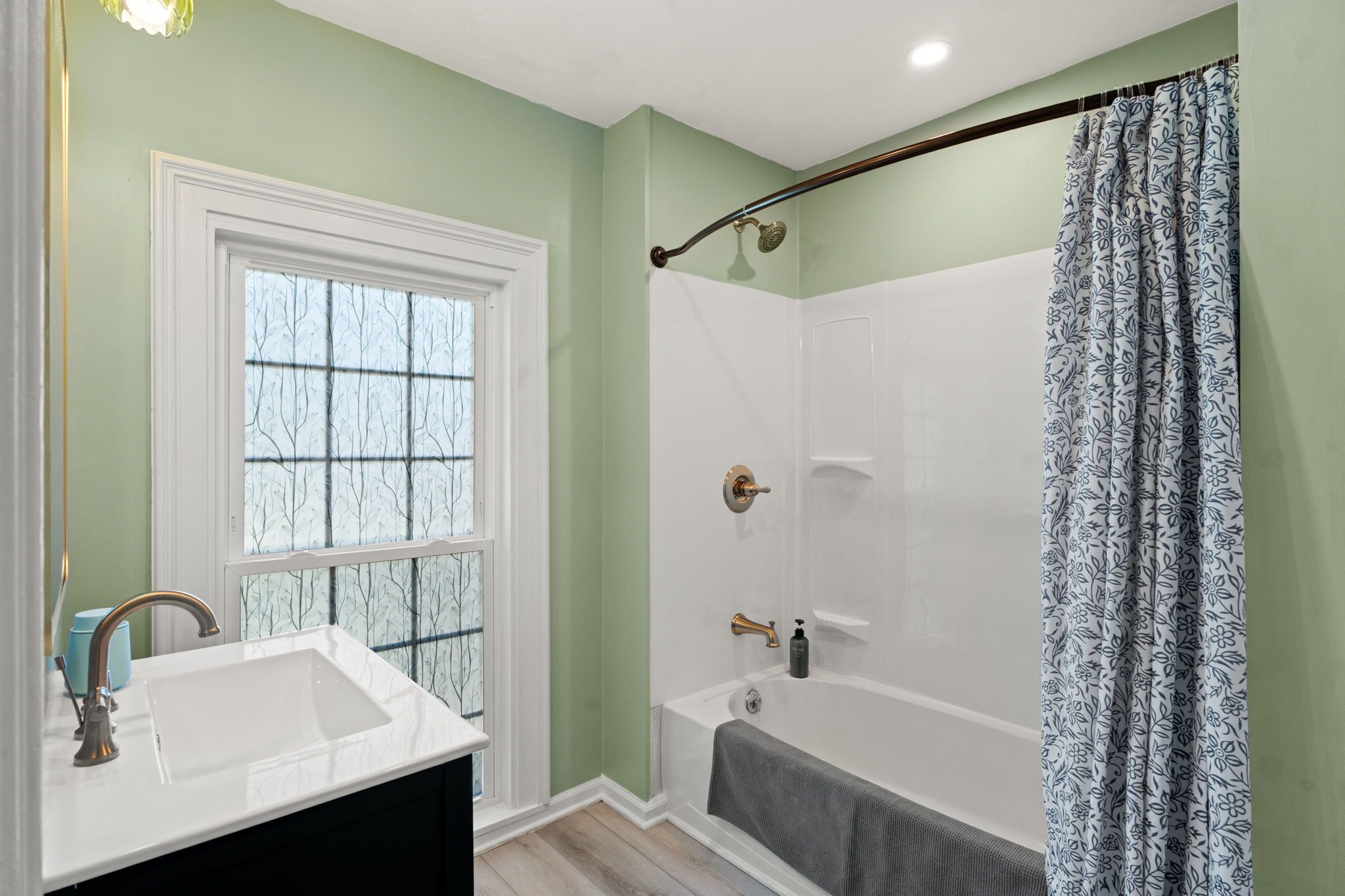 A bathroom with a white bathtub, a shower with a glass door, a window with frosted glass, and a sink with a faucet.