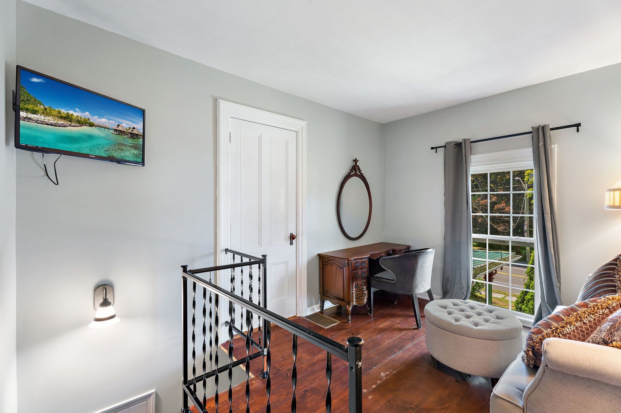 A room with a staircase, a desk, a chair, a sofa, a TV, and a window with curtains.