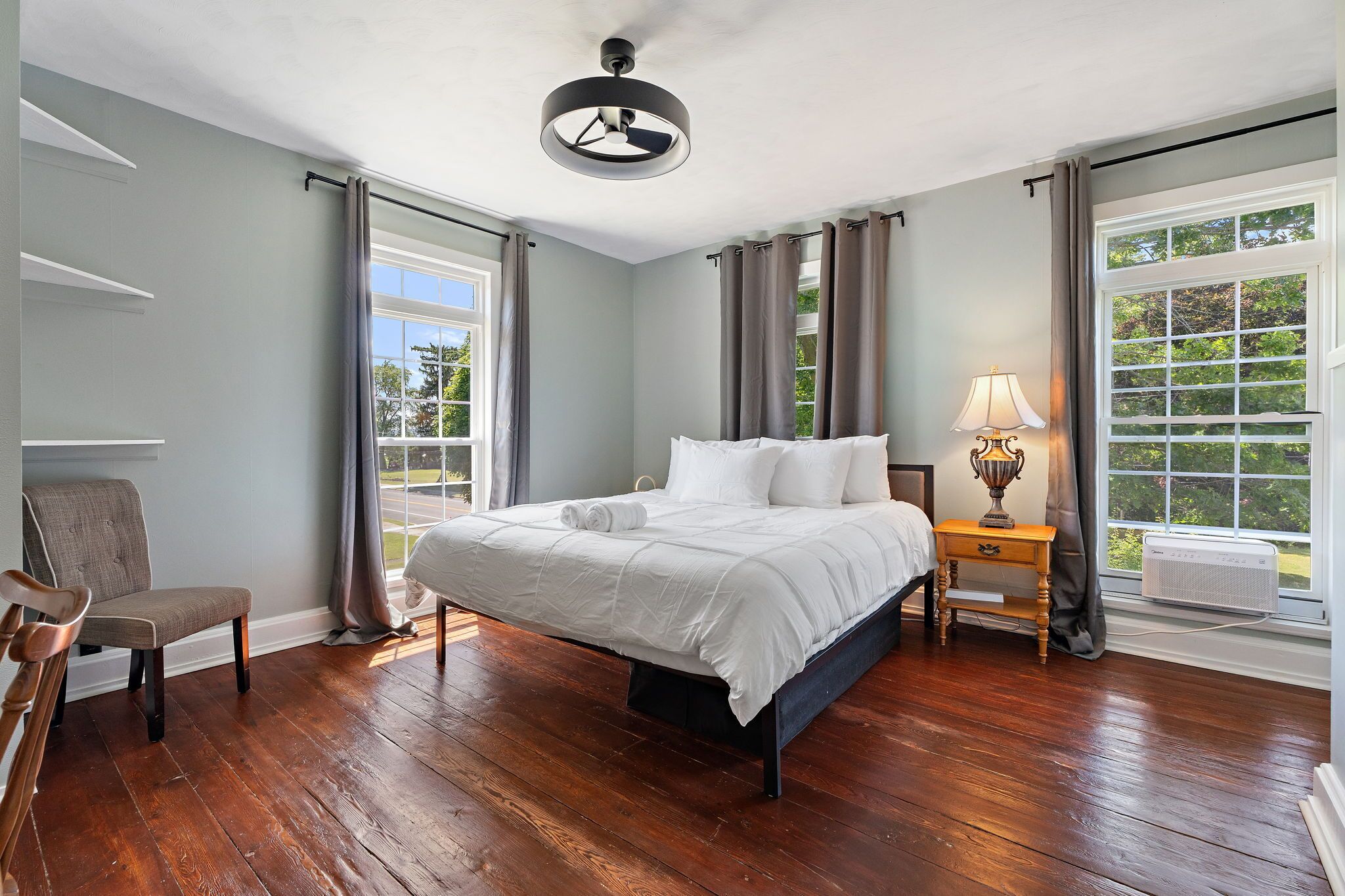 A hotel room with a large bed, a chair, a bedside table with a lamp, and a window with curtains.