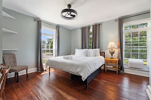 Habitación de hotel con una cama grande, una silla, una mesita de noche con lámpara y una ventana con cortinas.