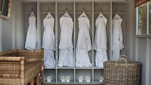 A walk-in closet with multiple shelves for folded towels and robes, a wicker chair, and a wicker basket. - Hilltop Shepherds Hut with Hot Tub and Tennis (Hambleden)