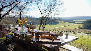 An outdoor dining setup with a table set for a meal, surrounded by trees and a scenic view of hills. - Hilltop Shepherds Hut with Hot Tub and Tennis (Hambleden)