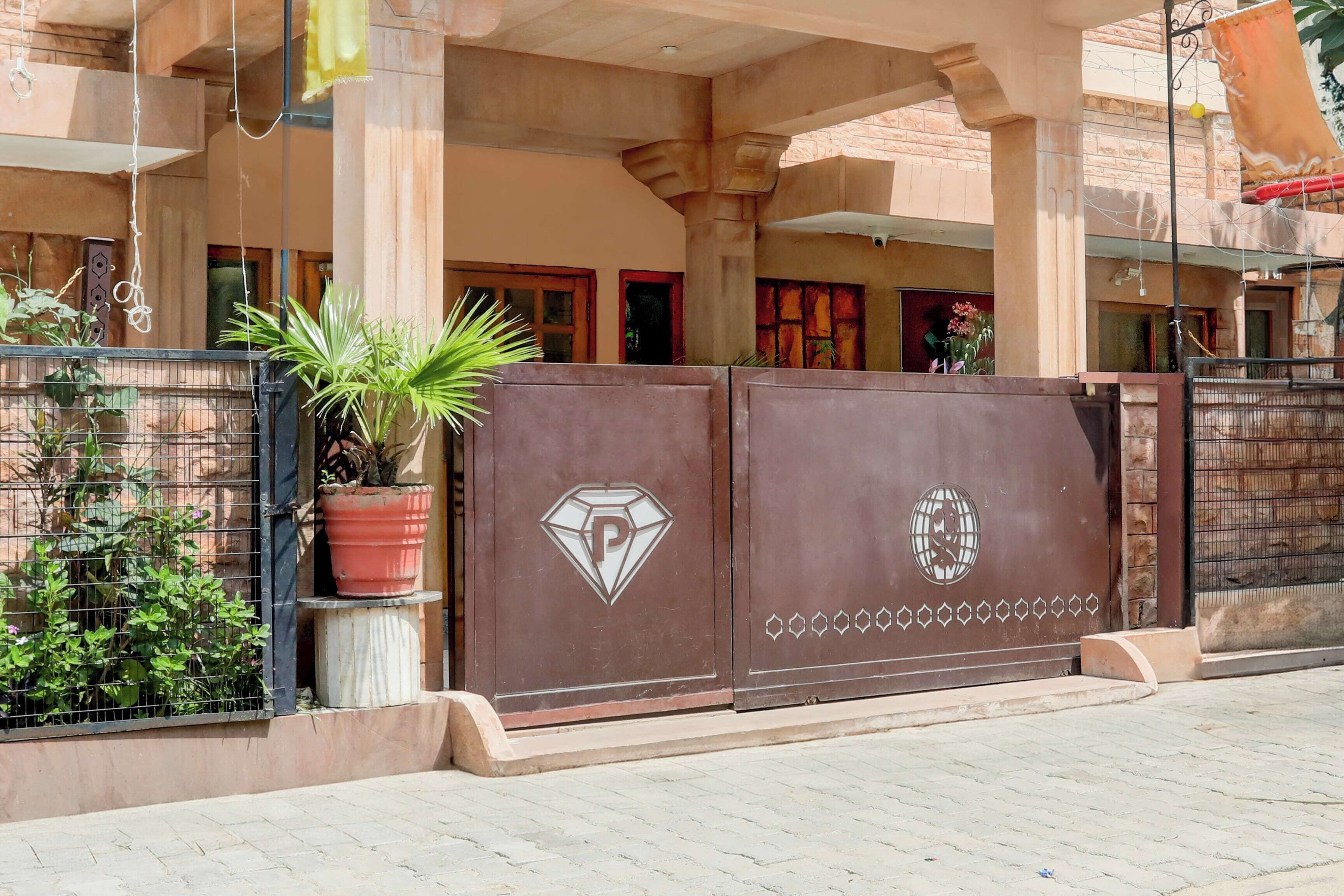 A gated entrance with a potted plant, a diamond-shaped emblem, and a globe symbol on the gate.