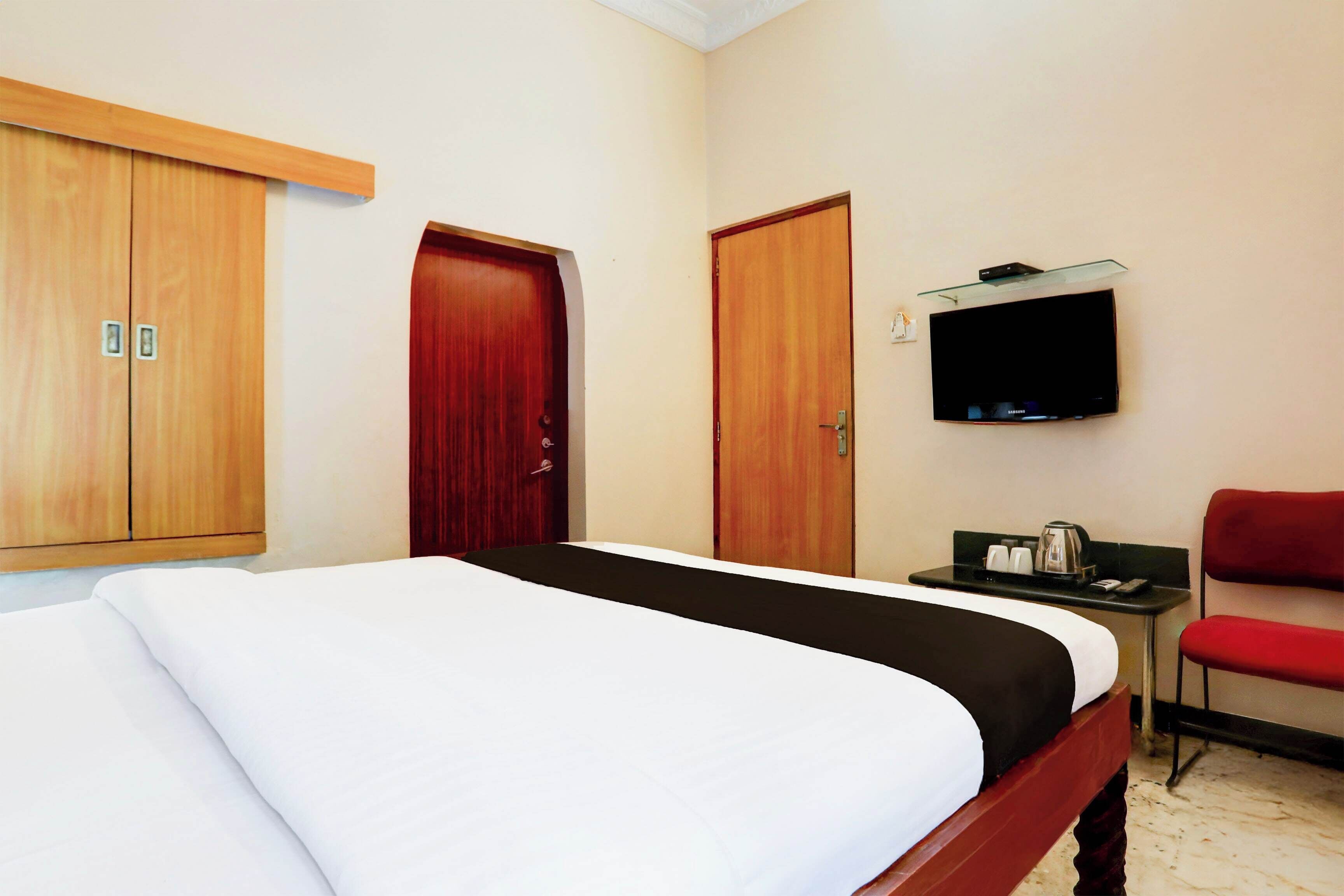 A hotel room with a bed, a desk with a television, and a red chair.