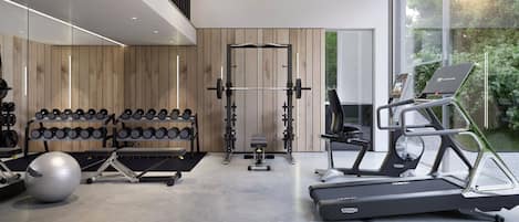 Un gimnasio moderno con diversos equipos, incluyendo mancuernas, una prensa de banca, un rack de sentadillas y máquinas de cardio.