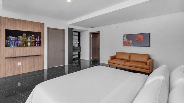 Ein modernes Hotelzimmer mit einem großen Bett, einer braunen Ledersofa, einem Stadtbild als Kunstwerk und einer schwarzen Regaleinrichtung.