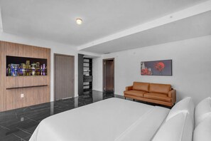 A modern hotel room with a large bed, a brown leather sofa, a cityscape artwork, and a black shelving unit. - Executive Miami Penthouse - 2bdr (Miami)