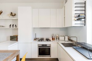 A modern kitchen with white cabinetry, a gas stove, an oven, a sink, and a wine rack. - Garibaldi's Residence (Milan)