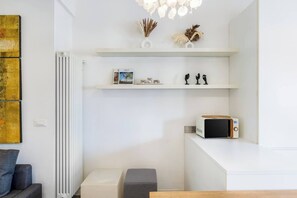 Een moderne woonkamer met een witte radiator, een bank, een salontafel en een magnetron op een wit aanrecht.